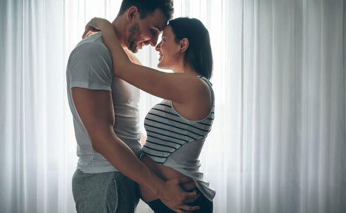 Side view of romantic couple standing by window at home