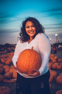 Portrait of smiling young woman holding pumpkin during sunset