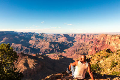 Rear view of man sitting on mountain against sky