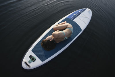 Woman lying in embryo pose on paddleboard over water
