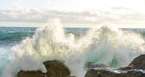 Panoramic view of waves splashing on sea against sky