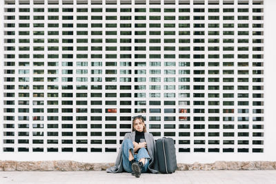 Full length portrait of a smiling young man sitting on brick wall