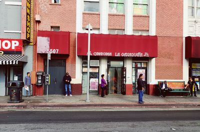 People walking on sidewalk by street against buildings in city