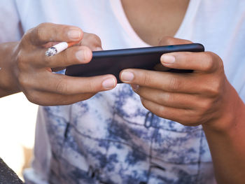 Midsection of man holding cigarette while using mobile phone