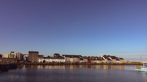 View of buildings by river against blue sky