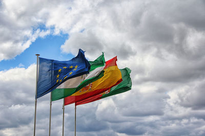 Low angle view of various flags against cloudy sky