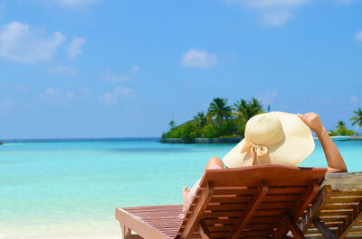 Woman relaxing on lounge chair at beach against sky