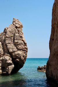 Rock formation by sea against clear blue sky