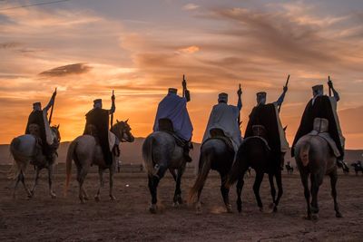 Rear view of people riding horses during sunset