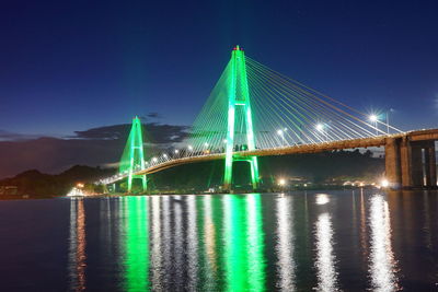 Illuminated bridge over river against sky at night