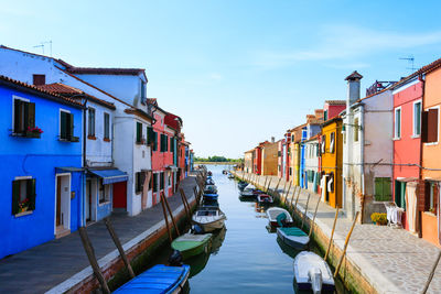 Boats moored in canal amidst buildings in city against sky