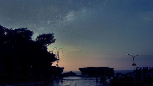 Silhouette trees by sea against sky at night