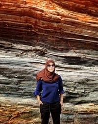 Portrait of young woman standing against rock formation