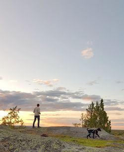 Rear view of man standing on street against sky during sunset