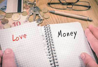 Cropped hands of person holding book with text by currency and keys on wooden table