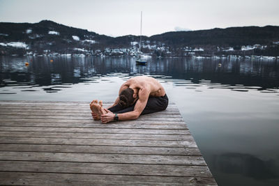 Man sitting on pier over lake against sky