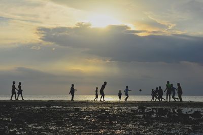 Silhouette people playing at beach against sky during sunset