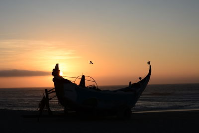 Silhouette boat moored on beach against sky during sunset