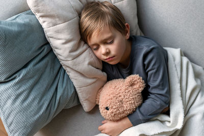 Preschool boy sleeps on the sofa in the living room, hugging his teddy bear.