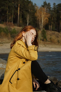 Beautiful woman in coat sitting at beach