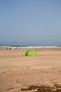 Green tent on the beach with few people walking around