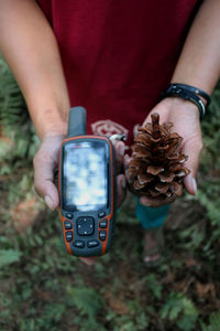 Midsection of man holding mobile phone and pine cone 