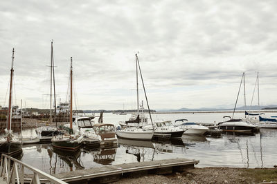 Sailboats moored at harbor against cloudy sky