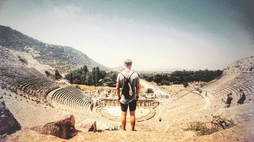 Rear view of man standing in old ruin against sky on sunny day