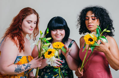 Smiling young women holding flowers against white background