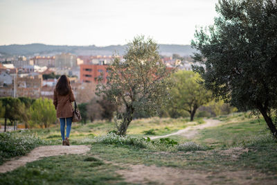 Rear view of woman walking on land by trees against sky