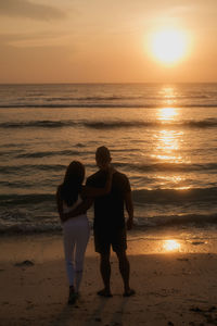 Rear view of couple walking at beach during sunset