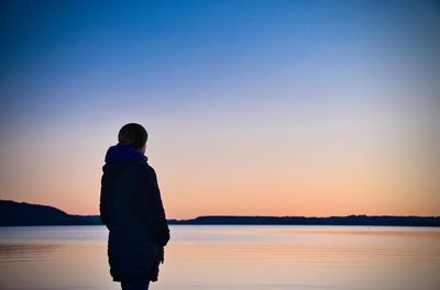 Woman looking at lake while standing against clear sky during sunset