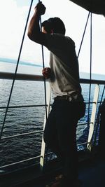 Man standing on swing at sea shore against sky