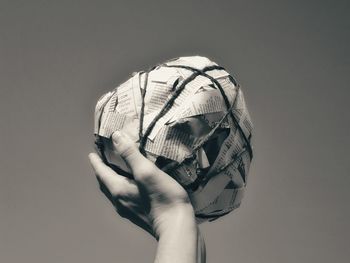 Cropped hand holding paper ball against sky