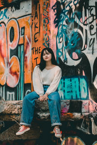 Full length of young man sitting against graffiti wall