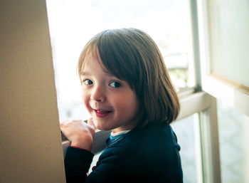 Portrait of cute girl standing by window at home