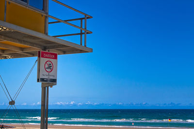 No swimming sign on lifeguard hut at beach against blue sky