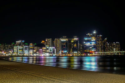 Illuminated buildings by river against sky at night