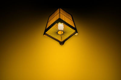 Low angle view of illuminated lamp hanging by yellow wall