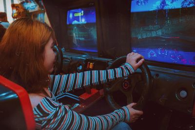 Girl sitting and playing a racing game on arcade