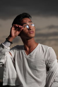 Young man wearing eyeglasses standing against sky