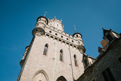 Low angle view of clock tower amidst buildings against clear blue sky