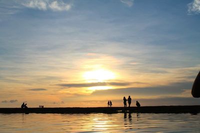 Silhouette people on beach against sky during sunset