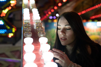 Portrait of woman looking at illuminated lighting equipment at night