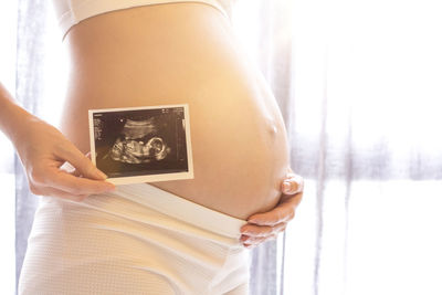 Midsection of pregnant woman holding sonogram