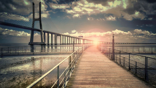 Suspension bridge over sea against sky during sunset