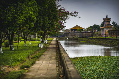 Footpath by lake and building against sky