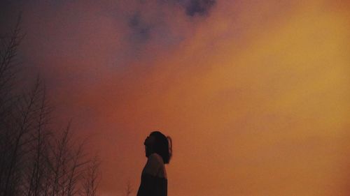 Silhouette woman standing by bare tree against sky during sunset