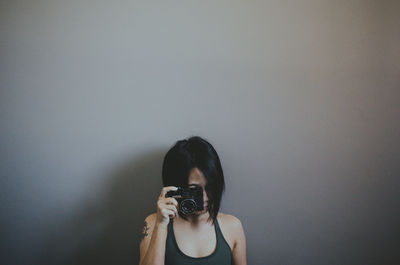 Portrait of woman photographing against wall