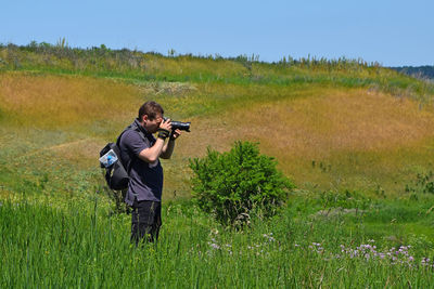 Photographer photographing on grassy field against clear sky